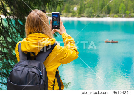 Tourist takes photo of the stunning lake Braies in the Dolomite mountains with turquoise water and wooden boats.  96104241