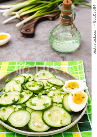 Sliced cucumber with green onions and boiled chicken egg on a plate on the table 96105594