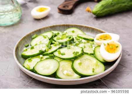 Ready-to-eat fresh cucumber salad, boiled chicken egg and green onions on a plate on the table Ready-to-eat fresh cucumber salad, boiled chicken egg and green onions on a plate on the table 96105598