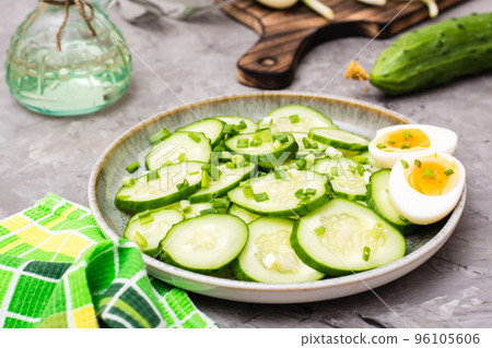 Fresh cucumber salad, boiled chicken eggs and green onions on a plate on the table 96105606
