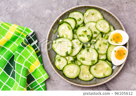 Ready-to-eat fresh cucumber salad, boiled chicken egg and green onions on a plate on the table. Top view Ready-to-eat fresh cucumber salad, boiled chicken egg and green onions on a plate on the table. Top view 96105612