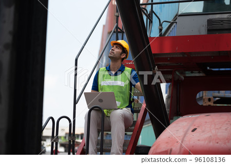 Young man working sitting on crane truck with computer at logistic import and export terminal industry.. 96108136