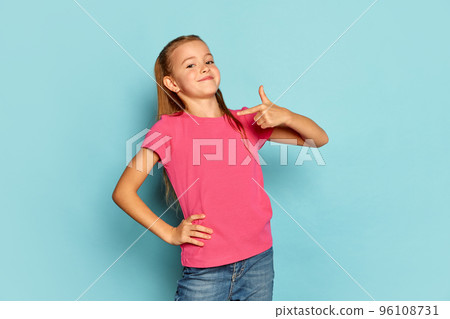 Portrait of little beautiful girl, child in pink T-shirt posing isolated over blue studio background. Proudly pointing at herself Portrait of little beautiful girl, child in pink T-shirt posing isolated over blue studio background. Proudly pointing at herself 96108731