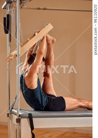 Fit man doing a lunge stretch yoga pilates exercise to strengthen and tone his muscles using a reformer in a gym 96110920