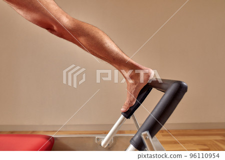 Side view of barefoot male athlete lying on pilates reformer and performing abs exercise during fitness workout. Pilates man concept. 96110954