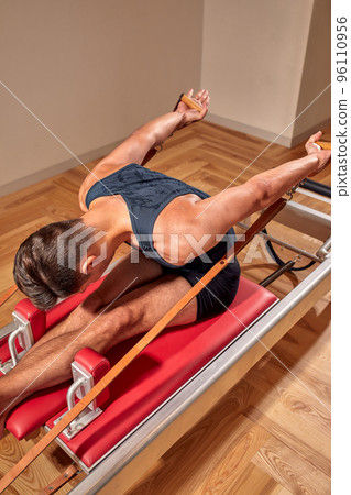 Fit man doing a lunge stretch yoga pilates exercise to strengthen and tone his muscles using a reformer in a gym 96110956