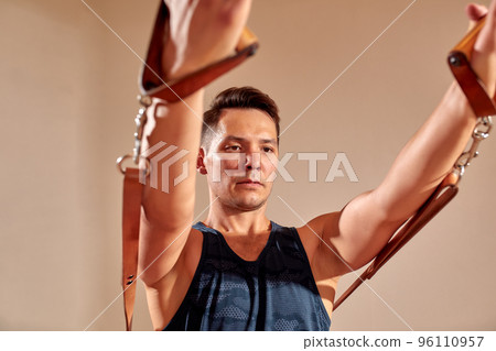 Side view of barefoot male athlete lying on pilates reformer and performing abs exercise during fitness workout. Pilates man concept. 96110957