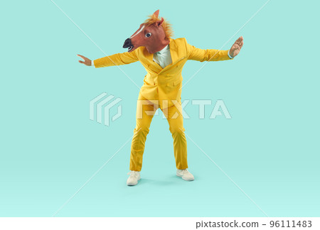 Funny happy man in yellow suit and horse mask dancing on turquoise studio background Funny happy man in yellow suit and horse mask dancing on turquoise studio background 96111483