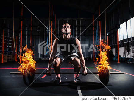 Athletic man works out at the gym with a fiery barbell Athletic man works out at the gym with a fiery barbell 96112659