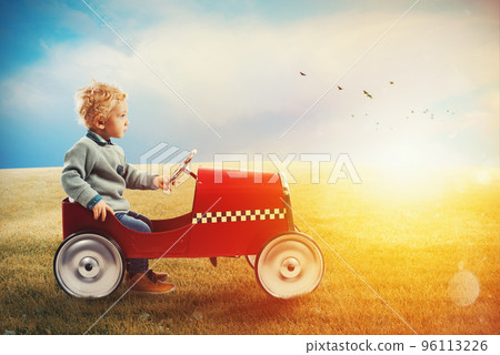 Child with car plays in a green field 96113226