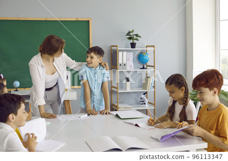 Friendly smiling teacher listens with pleasure to small schoolboy who answers at blackboard. 96113347