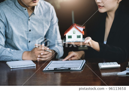 Concept of signing loan agreements, refinancing, buying and selling houses and land, focusing on model houses. A real estate agent is pointing to contract documents for male clients to Buy a dwelling Concept of signing loan agreements, refinancing, buying and selling houses and land, focusing on model houses. A real estate agent is pointing to contract documents for male clients to Buy a dwelling 96113658