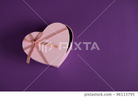 Still life. Top view composition with a half open heart shaped pink gift box with tied bow, isolated on violet background with copy ad space. Romantic present for Saint Valentine's or Women's Day 96113795