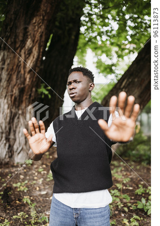Shocked young 20s African man wear casual streetwear in park outdoor, doing stop not me sign with palms of hands. Denial gesture and face expression. Fall or spring season 96113873