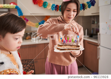 Boy sitting at the table and looking away while his mother putting candles at his birthday cake 96113928