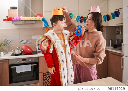 Caucasian woman putting paper crown at the head of her child with Down syndrome 96113929