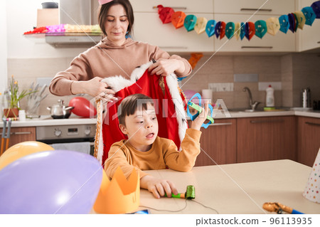 Woman wearing paper crown preparing celebrating birthday with her lovely son with genetic disorder Woman wearing paper crown preparing celebrating birthday with her lovely son with genetic disorder 96113935