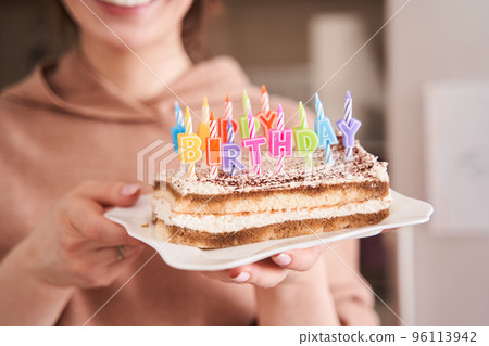 Mother holding birthday cake with colourful candles while preparing celebrating 96113942