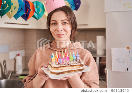 Caucasian woman holding birthday cake with colourful candles while preparing celebrating 96113943