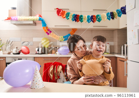 Woman and her son with Down syndrome playing at the kitchen with teddy bear toy 96113961