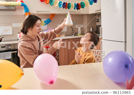 Caucasian woman putting party hat at her son with genetic disorder 96113965