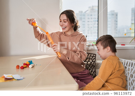 Friendly caucasian woman blowing soap bubbles with her son at the kitchen Friendly caucasian woman blowing soap bubbles with her son at the kitchen 96113972