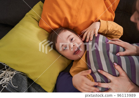 Little boy with down syndrome laying at the bed while his mother playing with him Little boy with down syndrome laying at the bed while his mother playing with him 96113989