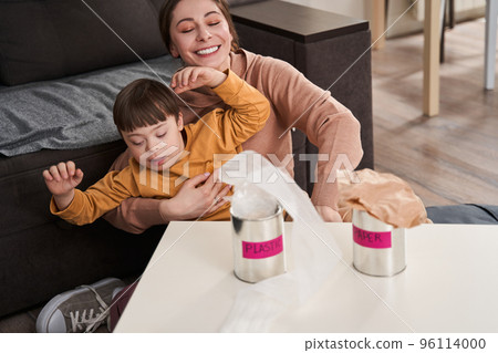 Mother and son with down syndrome in kitchen talking and sorting rubbish for recycling Mother and son with down syndrome in kitchen talking and sorting rubbish for recycling 96114000