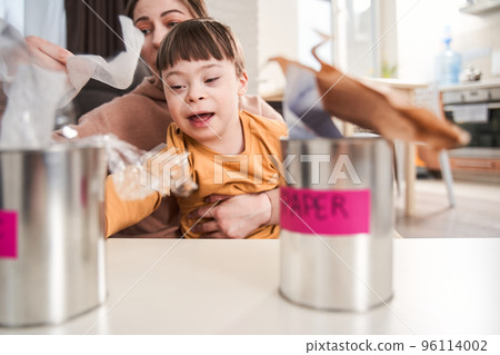 Kid with down syndrome sorting garbage near his mother at the table at home Kid with down syndrome sorting garbage near his mother at the table at home 96114002