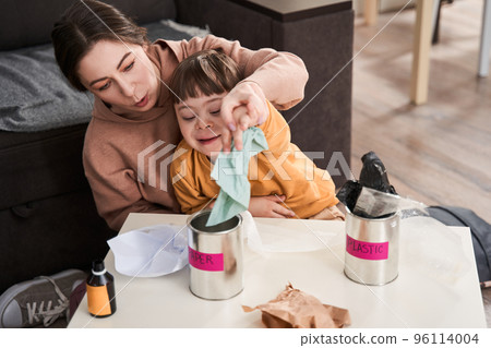 Mother and son with down syndrome sitting at the kitchen and sorting rubbish for recycling 96114004
