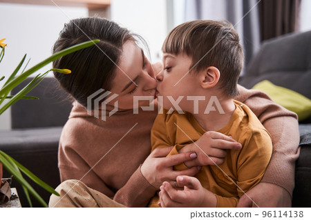 Woman kissing at the lips her son with down syndrome while sitting at home Woman kissing at the lips her son with down syndrome while sitting at home 96114138