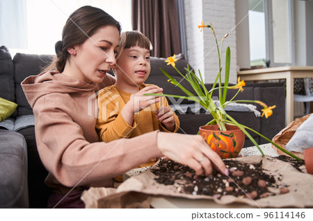 Mother replacing plants at the ground while sitting with her child with genetic disorder Mother replacing plants at the ground while sitting with her child with genetic disorder 96114146