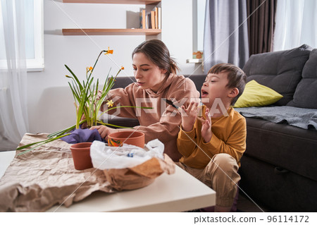 Woman transplanting flowers while sitting on the floor at home and chatting with her son Woman transplanting flowers while sitting on the floor at home and chatting with her son 96114172