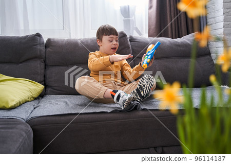 Little boy with Down syndrome sitting at the sofa with his toy gun while relaxing 96114187