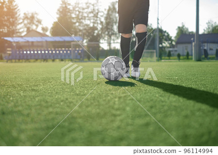 A boy in a professional uniform and cleats runs after a soccer ball making a pass on a football field with artificial grass flooring. Youth soccer lessons at the stadium. 96114994