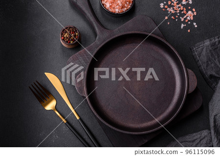 Brown iron empty pan with kitchen utensils on a dark concrete background Brown iron empty pan with kitchen utensils on a dark concrete background 96115096
