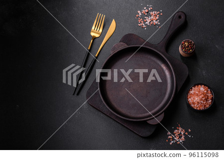 Brown iron empty pan with kitchen utensils on a dark concrete background Brown iron empty pan with kitchen utensils on a dark concrete background 96115098