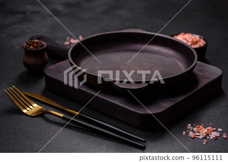 Brown iron empty pan with kitchen utensils on a dark concrete background Brown iron empty pan with kitchen utensils on a dark concrete background 96115111