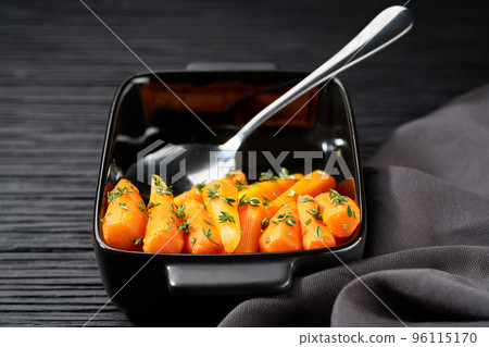 baked honey glazed baby carrots with thyme in a ceramic form on a dark wooden table, selective focus. baked honey glazed baby carrots with thyme in a ceramic form on a dark wooden table, selective focus. 96115170
