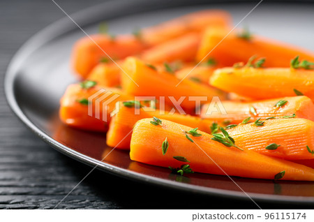 Baked (roasted) honey glazed baby carrots with thyme on a dark ceramic plate, macro shot. 96115174