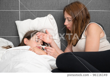 Mother measuring temperature of her ill daughter. Sick child with high fever laying in bed and 96116149