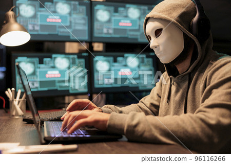 Impostor with mask hacking computer network at night, working on laptop and multiple monitors to steal IT information. Masked hacker with hidden identity acting dangerous, security breach. Impostor with mask hacking computer network at night, working on laptop and multiple monitors to steal IT information. Masked hacker with hidden identity acting dangerous, security breach. 96116266