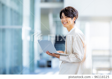 Young man standing with laptop in office lobby 96118125