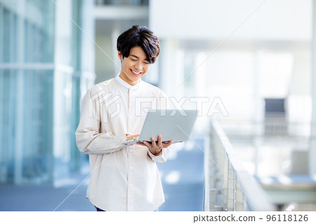 Young man standing with laptop in office lobby 96118126