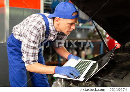 Mechanic with laptop near car engine in auto service Mechanic with laptop near car engine in auto service 96119674