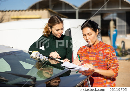 Two women signing agreement while standing at car outdoors Two women signing agreement while standing at car outdoors 96119705