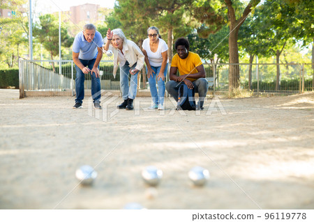 A group of multiracial mature adult people playing patanque game outdoors in a park A group of multiracial mature adult people playing patanque game outdoors in a park 96119778