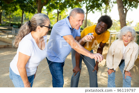 Carefree multiracial friends throwing metal balls on a sandy background in the park 96119797