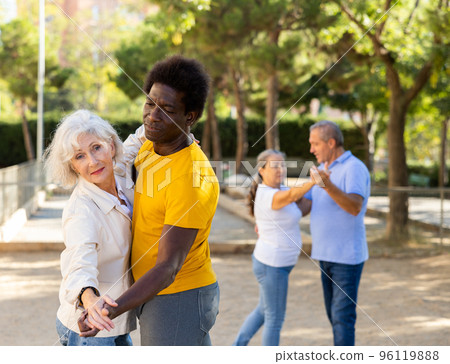 Cheerful multiracial middle aged and older adults enjoying dancing in pairs outdoor at park 96119888