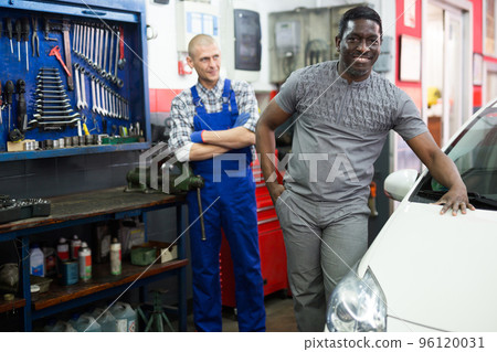 Portrait of satisfied male client with mechanician standing near her car after repairing in workshop Portrait of satisfied male client with mechanician standing near her car after repairing in workshop 96120031